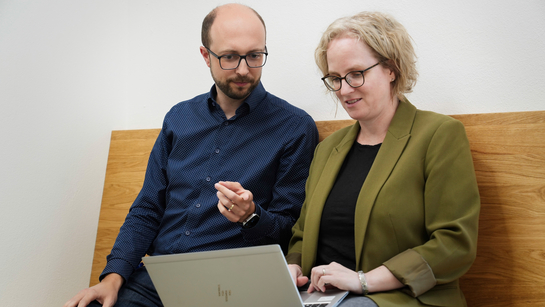 Ein Mitarbeiten und eine Mitarbeiterin mit Notebook tauschen sich in lockerer Atmosphäre aus