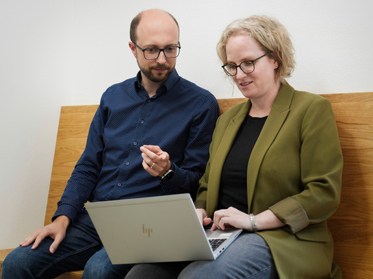 Ein Mitarbeiten und eine Mitarbeiterin mit Notebook tauschen sich in lockerer Atmosphäre aus