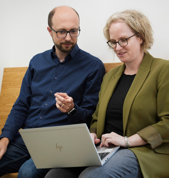 Ein Mitarbeiten und eine Mitarbeiterin mit Notebook tauschen sich in lockerer Atmosphäre aus