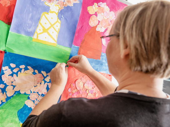 Eine Lehrperson hängt Kinderzeichnungen an die Wand