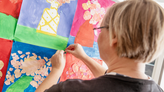 Eine Lehrperson hängt Kinderzeichnungen an die Wand