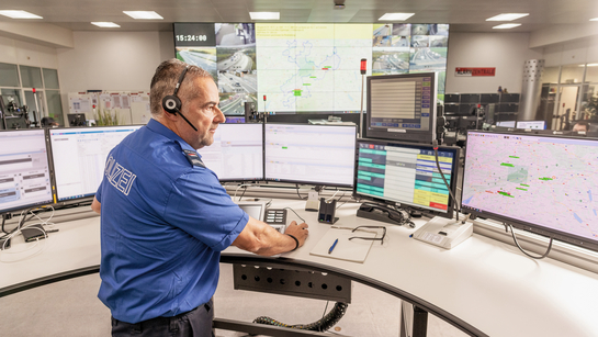 Ein Polizist arbeitet vor vielen Bildschirmen und sorgt so für Sicherheit