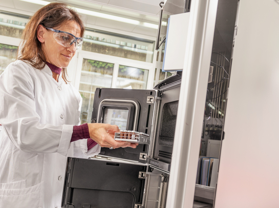 Eine Mitarbeiterin des Gesundheitsamtes entnimmt etwas aus einem Laborschrank