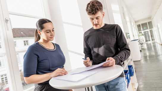 Zwei junge Mitarbeitende des Rechtsdienst sprechen am Stehtisch