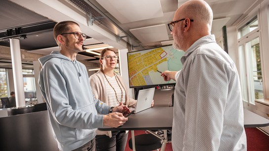 Drei Mitarbeitende unterhalten sich am Stehpult zur Karte Geoinformationen