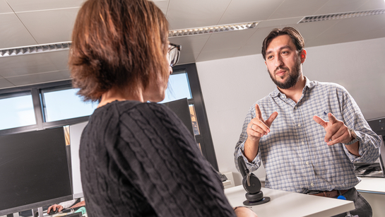 Eine Mitarbeiterin und ein Mitarbeiter aus dem Bereich IT unterhalten sich über den Schreibtisch