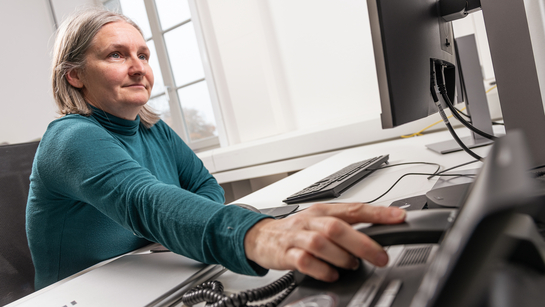 Eine Mitarbeiterin sitzt am Schreibtisch und nimmt Anrufe entgegen