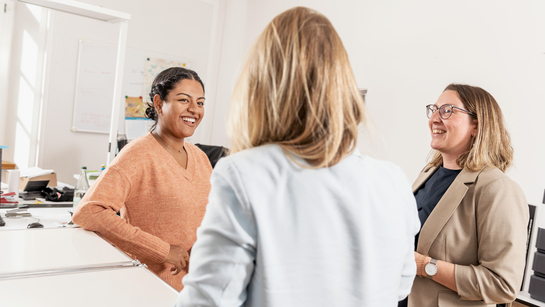 Drei Mitarbeiterinnen unterhalten sich wohlwollend zusammen im Büro
