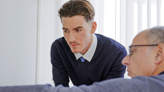 Ein Mitarbeiter aus dem Steueramt erklärt dem Lernenden etwas am Bildschirm