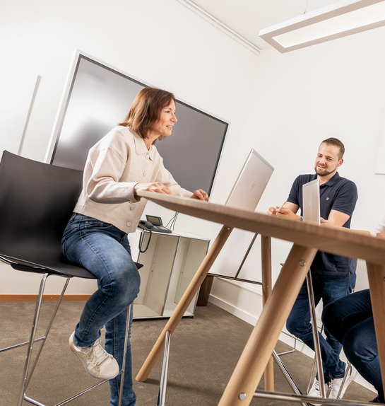 Drei Mitarbeitende kommunizieren an einem hohen Tisch