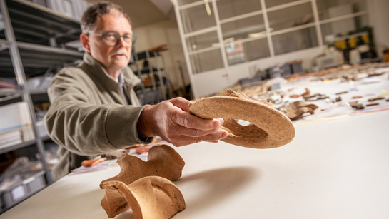 Ein Mann aus dem Amt für Denkmalpflege und Archäologie sortiert an einem Tisch Tonfunde aus Ausgrabungen