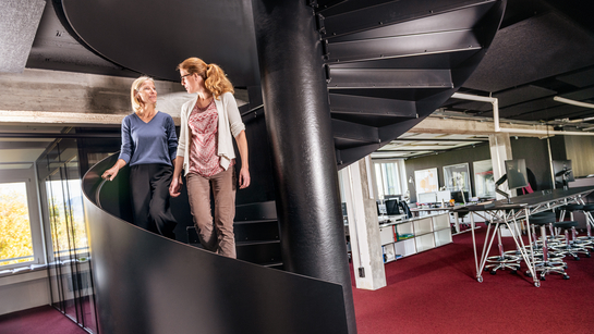 Zwei Mitarbeitende des Hochbauamts unterhalten sich auf einer schwarzen Wendeltreppe