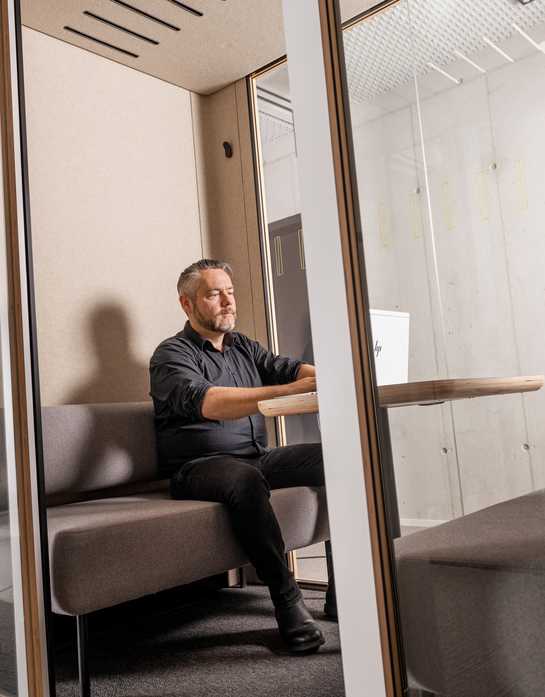 Ein IT-Mitarbeiter sitzt im Sitzungszimmer hinter Glastüren