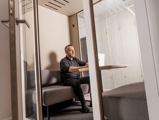 Ein IT-Mitarbeiter sitzt im Sitzungszimmer hinter Glastüren