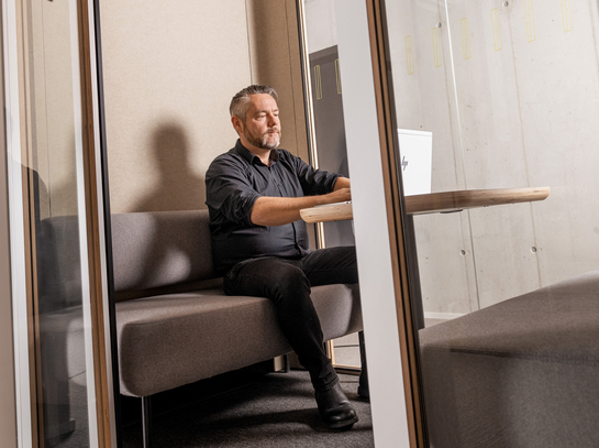 Ein IT-Mitarbeiter sitzt im Sitzungszimmer hinter Glastüren
